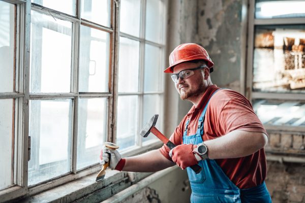 Professional worker, in uniform and goggles, beats old plaster from a brick wall