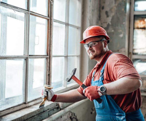 Professional worker, in uniform and goggles, beats old plaster from a brick wall