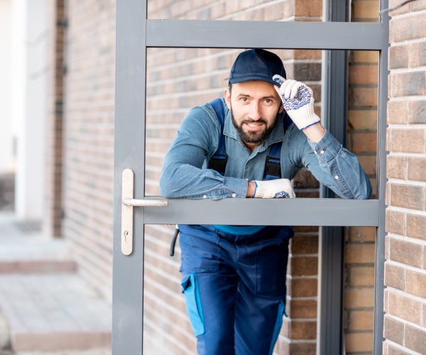 Funny portrait of a builder looking through the entrance door of a new house outdoors