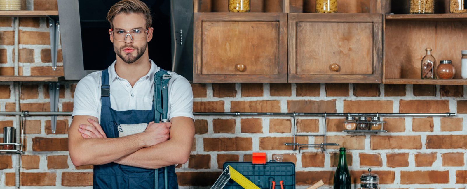 handsome young professional repairman with tool belt standing with crossed arms and looking at
