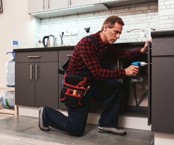 Handyman at work. Repairing kitchen shelves by perforator. Artisan senior adult man trying to fix kitchen shelves