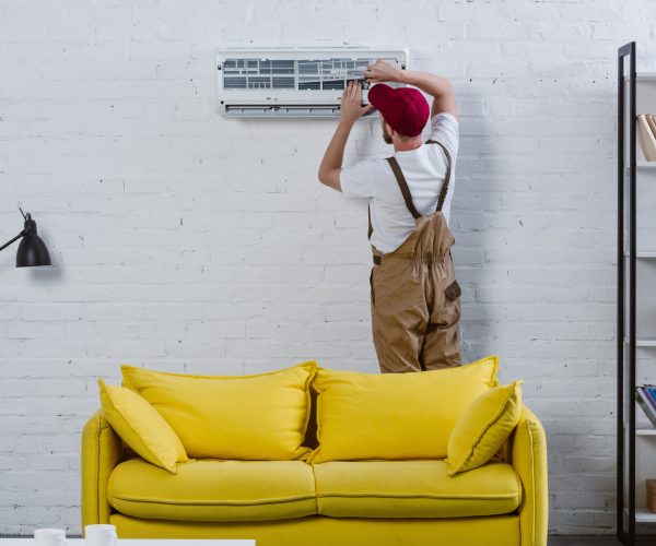 professional repairman fixing air conditioner hanging on white brick wall
