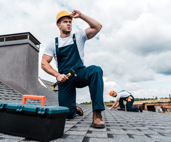 selective focus of handsome handyman touching helmet while holding hammer
