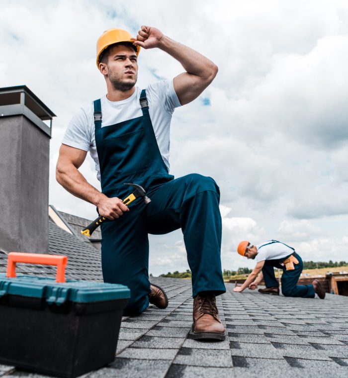 selective focus of handsome handyman touching helmet while holding hammer