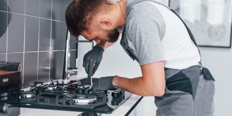 Young professional plumber in grey uniform working on the kitchen.